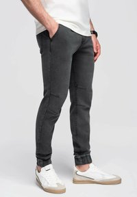 Pantalones jogger ajustados grises, confeccionados en denim, con detalles de costura en las rodillas y puños elásticos, combinados con zapatillas blancas.
