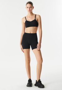 Zwart sportoutfit met een aansluitende crop top met dunne bandjes en hooggesneden shorts. Glad materiaal met een strakke, minimalistische uitstraling.