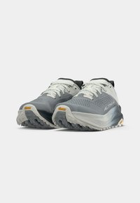 Une paire de chaussures de sport grises et blanches avec des semelles Vibram et des lacets, vue de face en angle sur un fond blanc.