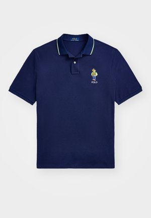 Polo de color azul marino hecho de algodón, con un cuello acanalado que presenta acentos en verde y blanco y un logo bordado en el lado izquierdo del pecho.