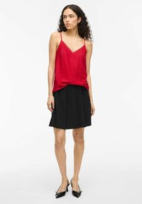 Rode satijnen camisole met kantafwerking, gecombineerd met een zwarte geplooide rok en zwarte slingback hakken. Glad textiel bovenop, gestructureerde rok.