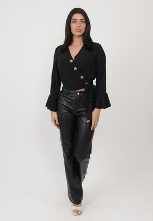 Blouse noire à manches cloche avec boutons en bois, associée à un pantalon en cuir noir taille haute et des sandales à talons transparents.
