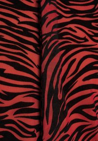 Tessuto rosso con un audace motivo a strisce nere di tigre, con una superficie testurizzata che crea profondità e interesse visivo.