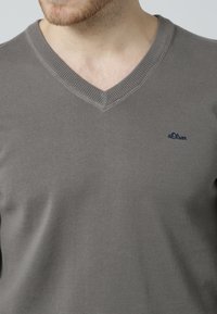 Grauer V-Ausschnitt-Pullover aus Strickstoff mit gerippten Bündchen und Saum, mit kleinem marineblauen Logo auf der linken Brust.