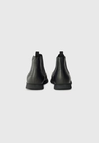 Bottines en cuir noir avec une finition texturée, des panneaux latéraux élastiques et des semelles en caoutchouc. Elles sont dotées d'une languette à l'arrière pour un enfilage facile.