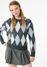 Szary sweter w wzór argyle z niebieskimi i białymi diamentami, o dzianinowej fakturze, okrągły dekolt; w połączeniu z plisowaną szaro-skalną spódnicą.