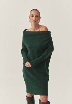 Roheline õlgadelt avatud kleit, mis on valmistatud pehmest, tekstureeritud kangast, pikad varrukad ja vabalt langev lõige. Kleit on kombineeritud põlveni ulatuvate mustade saapadega.