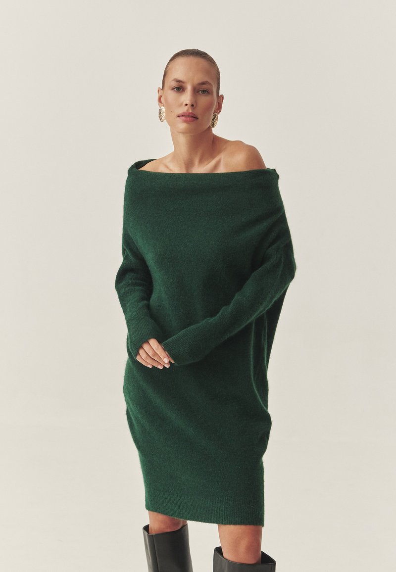 Roheline õlgadelt avatud kleit, mis on valmistatud pehmest, tekstureeritud kangast, pikad varrukad ja vabalt langev lõige. Kleit on kombineeritud põlveni ulatuvate mustade saapadega.