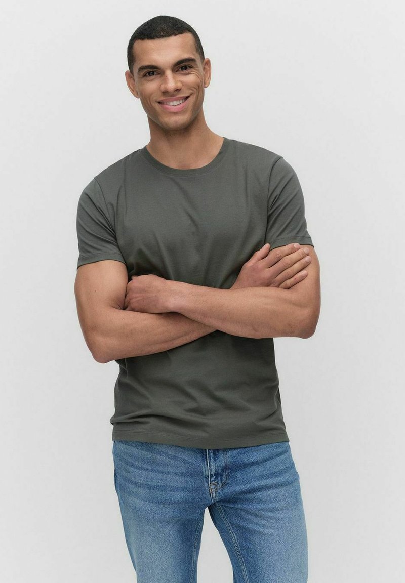 Oliwkowa koszulka z krótkim rękawem o dopasowanym kroju, noszona z niebieskimi dżinsami. Gładki materiał z okrągłym dekoltem i podwiniętymi mankietami.