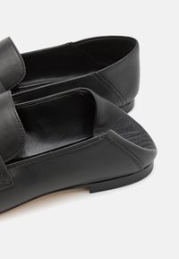 Zwarte leren schoenen met open achterkant, een gladde textuur en minimale stiksels. Voorzien van een ronde neus en een platte zool.