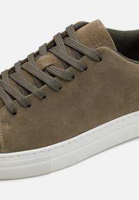 Semskinn joggesko i olivengrønn farge med matchende flate snører. Har en hvit gummisåle, minimal søm og avrundet tådesign.