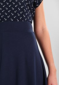 Haut bleu marine avec imprimé d'ancre blanche, associé à une jupe bleu marine unie. Texture lisse avec une taille ajustée et un design de jupe fluide.