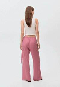 Lichtroze wijde broek met elastische tailleband, gecombineerd met een witte mouwloze top met textuur. Glad materiaal en ontspannen pasvorm.