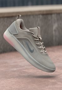 Sapatilha desportiva bege claro com parte superior em malha, acabamentos texturizados, uma sola translúcida e um logótipo subtil de lado. Design de bico arredondado.