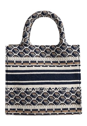 Sac cabas en tissu tissé avec des motifs géométriques bleu marine, blanc et beige, incluant des rayures et des formes d'éventail, avec deux poignées courtes.