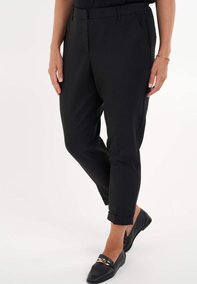 Pantalones negros a medida hechos de un tejido ligero, con un corte slim, dobladillos con puños y bolsillos laterales. Combinados con mocasines negros.