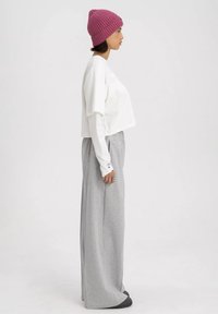 Witte cropped shirt gelaagd over een lange mouw top, gecombineerd met grijze wijdvallende sweatpants en een roze ribgebreide beanie. Soepele texturen overal.