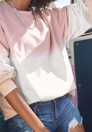 Sudadera ligera con bloques de color que presenta un degradado de rosa suave a blanco, con cuello redondo y puños acanalados, combinada con pantalones cortos de mezclilla.