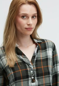 Karierte Hemd in Dunkelgrün, Grau und Orange mit einem geknöpften Kragen, weicher Textur und sichtbarer Knopfleiste.