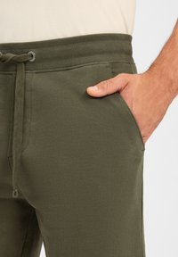 Olivgrüne Jogginghosen mit Kordelzug, Rippbündchen und seitlichen Taschen, aus weichem, dehnbarem Baumwollstoff.
