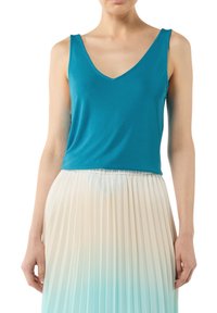 Turkusowy top bez rękawów z dekoltem w kształcie litery V, wykonany z gładkiego materiału. W zestawieniu z plisowaną spódnicą w gradientzie przechodzącym od kremowego do jasnoniebieskiego.