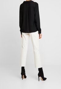 Chemise noire à manches longues avec col, associée à un pantalon ajusté blanc cassé et des bottines noires à talons. Design simple, texture lisse et coupe ajustée.