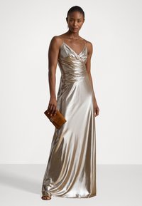 Metallinen kultainen maksimekko, jossa on istuva bodice, röyhelömuotoilu ja naruolkaimet. Yhdistetty ruskeaan clutch-laukkuun, jossa on pyöreä korostus.