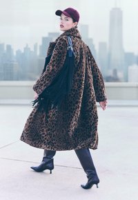 Leopardmønstret faux fur frakke med høj krave, parret med en maroon kasket og sorte hæle støvler. Har en frynsedekoreret sort clutch.