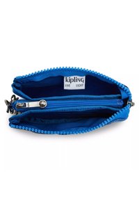 Blå tygmyntpung med dragkedjestängning, featuring en texturerad dragkedja vid kanten och en inre dragkedjeficka. Synliga etiketter: "kipling" och "LIVE LIGHT."
