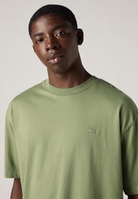T-shirt in cotone verde con maniche corte, collo rotondo e piccolo logo sul petto. Tessuto morbido, vestibilità rilassata, design minimale.