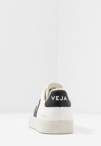 Bijela kožna tenisica s crnim akcentima i teksturiranim bočnim dijelom. Sadrži "VEJA" branding u bijeloj boji na stražnjem dijelu. Gumeni potplat, minimalistički dizajn.