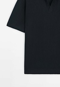 Chemise tricotée noire à manches courtes avec col en V et texture côtelée, posée à plat sur fond blanc.