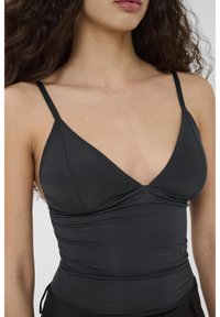 Débardeur noir ajusté avec bretelles fines réglables, encolure en V, détail de tissu froncé et texture lisse. Convient pour être porté en superposition.