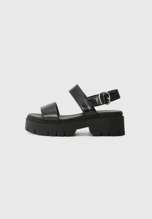 Sandali platform neri in pelle con due ampie cinghie, fibbia regolabile alla caviglia e una suola spessa in gomma con un motivo seghettato.