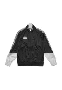 Chaqueta de chándal negra y gris con cremallera frontal, puños elásticos y dos bolsillos laterales. Presenta patrones geométricos blancos a lo largo de los hombros.