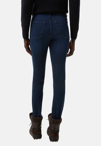 Tmavě modré džíny se slim fit, s zadními kapsami, vyrobené z denimu. Nosené s hnědými botami s kožešinovým podšívkou.