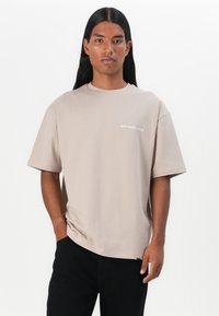 Beige kortærmet t-shirt med rund halsudskæring og afslappet pasform. Har hvid tekst "don't waste culture" på venstre side.