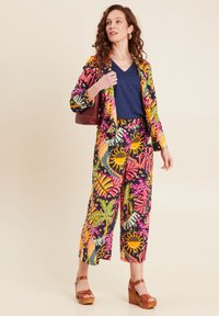 Kleurrijk bloemenprint pak met een marineblauwe top, bestaande uit wijde broekspijpen en een aansluitende blazer, gecombineerd met bruine houten plateau schoenen.