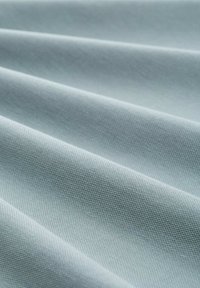 Lysblåt stof med en tekstureret overflade, foldet i læg, der viser et glat, slidstærkt materiale og en ensartet farve gennem hele stoffet.