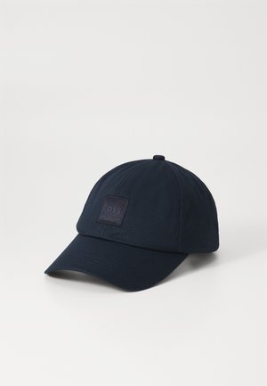 Gorra de béisbol azul marino hecha de tela suave, con una corona estructurada, visera curvada y un parche de logo cuadrado en la parte frontal.