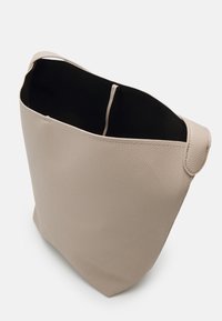 Sac seau en cuir beige avec une bandoulière unique et une doublure intérieure noire visible, présenté sous un angle latéral supérieur.