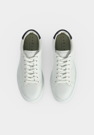 Paire de baskets blanches à lacets avec col de talon rembourré noir, semelles texturées et semelles intérieures de marque sur fond blanc uni.