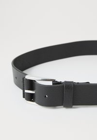 Black leather belt with silver metal buckle laid flat on a white surface, showing belt holes and leather loop detail.