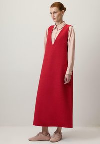 Červené textúrované šaty bez rukávov s hlbokým V-výstrihom, nosené over light pink košeľou s golierom. V kombinácii s bledoružovými teniskami.