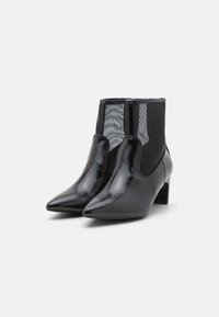Botines negros de punta afilada con un acabado brillante, que cuentan con paneles elásticos en los laterales y un tacón de bloque de altura media. Parte trasera texturizada para un detalle adicional.