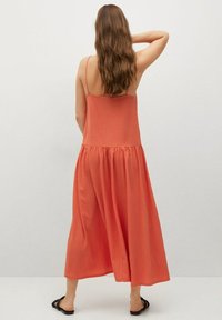 Robe maxi en corail orange, avec des bretelles fines, un corsage ajusté et une jupe fluide et froncée. Le tissu a une finition texturée.
