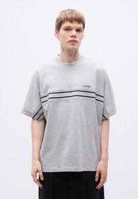 Γκρι βαμβακερό T-shirt με κοντά μανίκια, με μαύρες οριζόντιες ρίγες και λογότυπο στο στήθος. Χαλαρή εφαρμογή και στρογγυλή λαιμόκοψη.