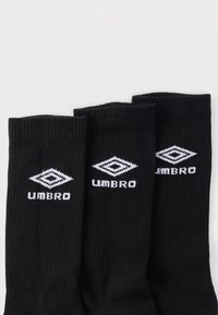 Fekete bordázott zoknik fehér "UMBRO" logóval és gyémántmintával. A szövet rugalmasnak tűnik, sima textúrájú. Három párból álló szett.