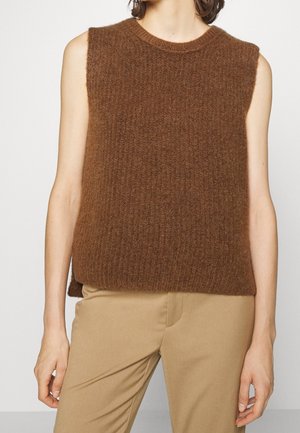 Gilet en tricot marron sans manches porté par-dessus un pantalon beige, montrant la taille et les bras sur un fond uni.