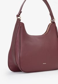 Borsa in pelle bordeaux con finitura testurizzata, forma curva e dettagli in zip dorato. Presenta un manico corto e un marchio discreto.